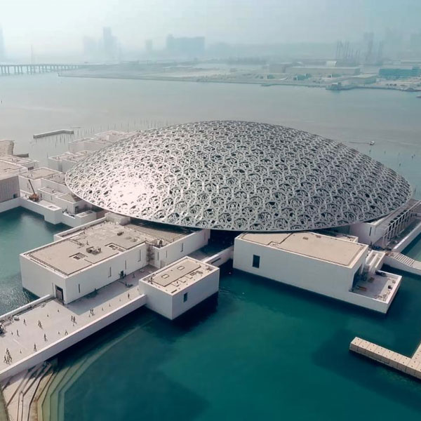 The Louvre Abu Dhabi — a mass covered by a perforated steel dome that transforms light into an architectural element, establishing a dialogue with the sea and the surrounding cultural space.